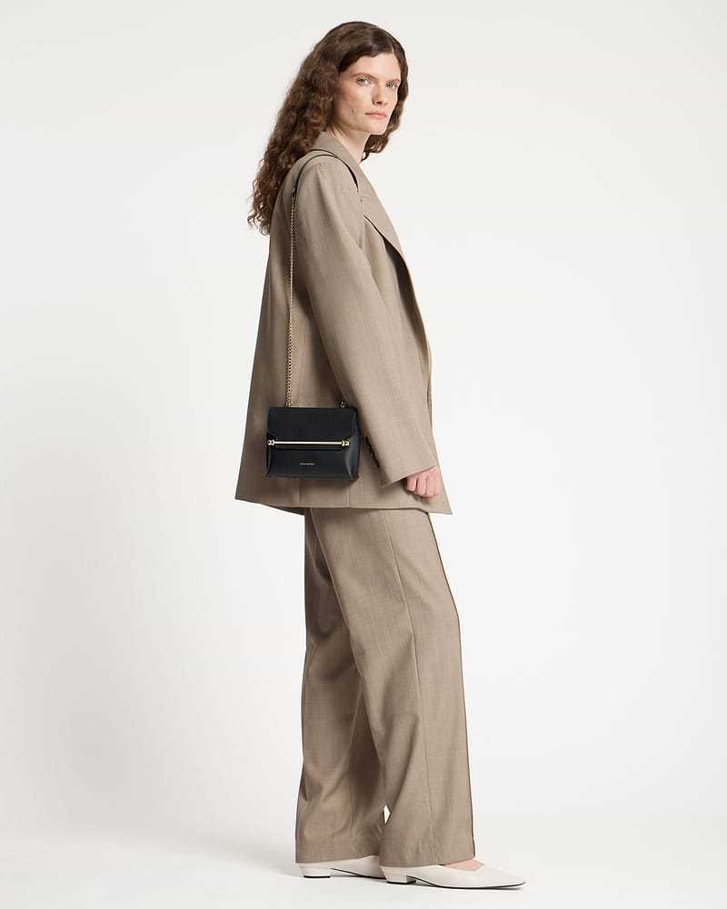 Model wearing a beige suit with a black Strathberry Stylist Mini shoulder bag.