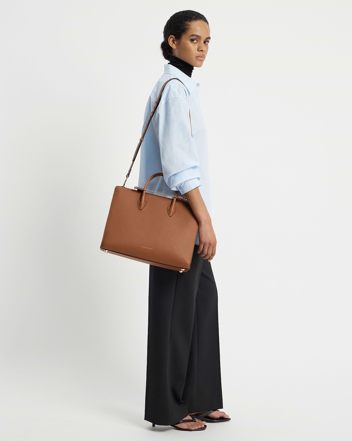 Model wearing a light blue shirt carrying a Strathberry chestnut leather tote.