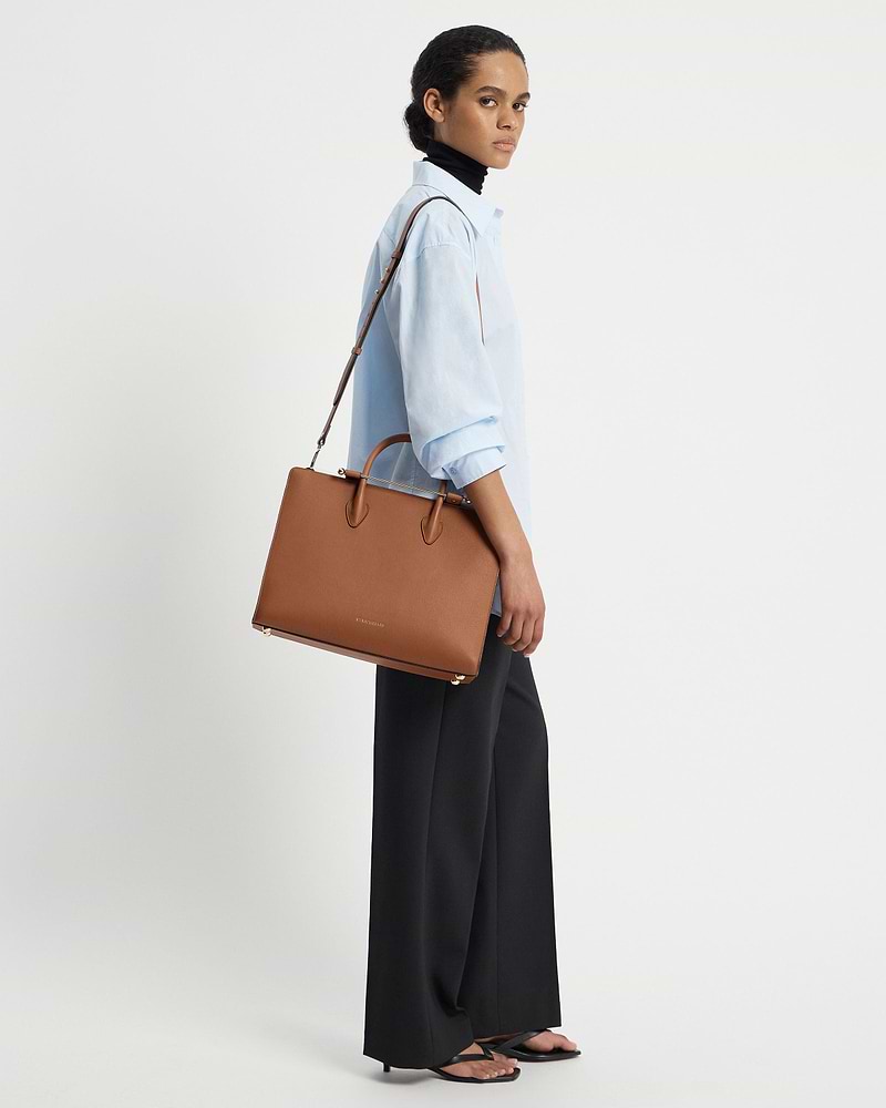 Model wearing a light blue shirt carrying a Strathberry chestnut leather tote.