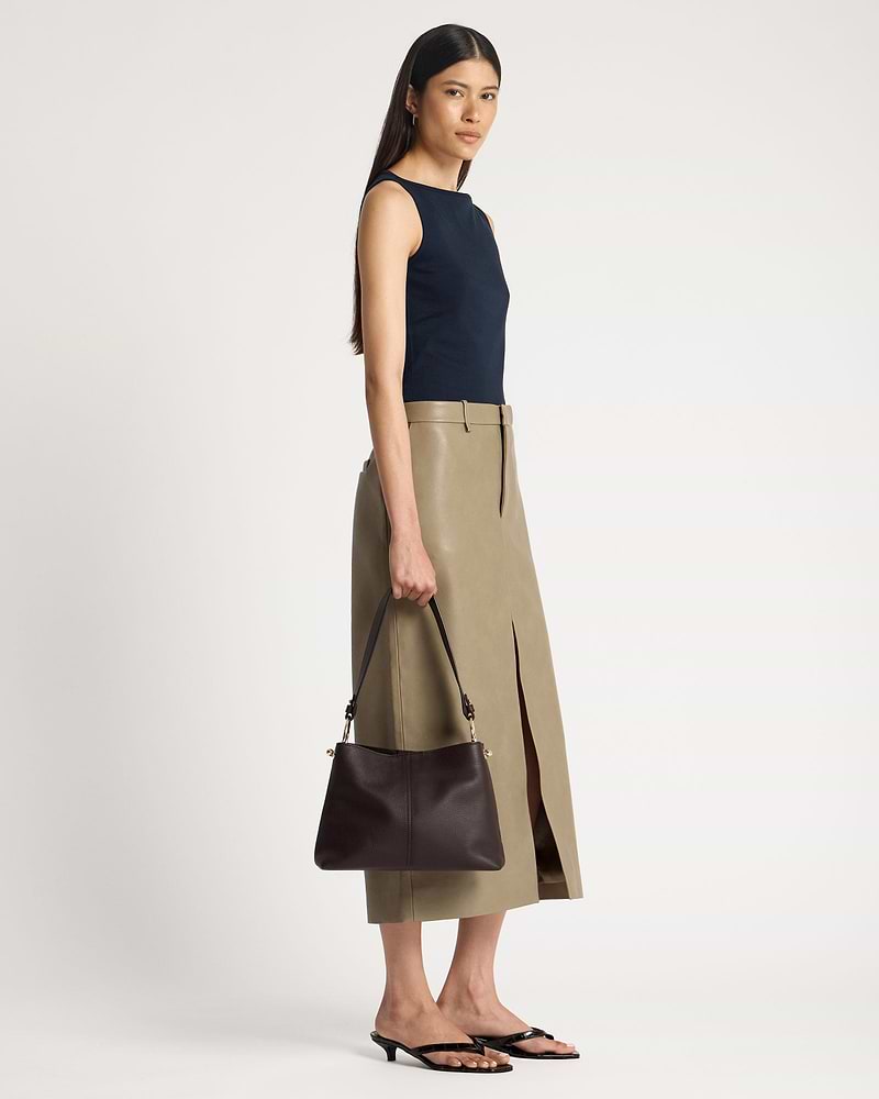 Model holding espresso leather hobo bag at her side, strap and hardware visible.