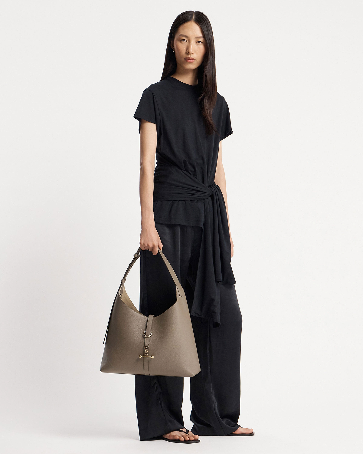 Model in a black outfit holding a taupe hobo bag with gold hardware.
