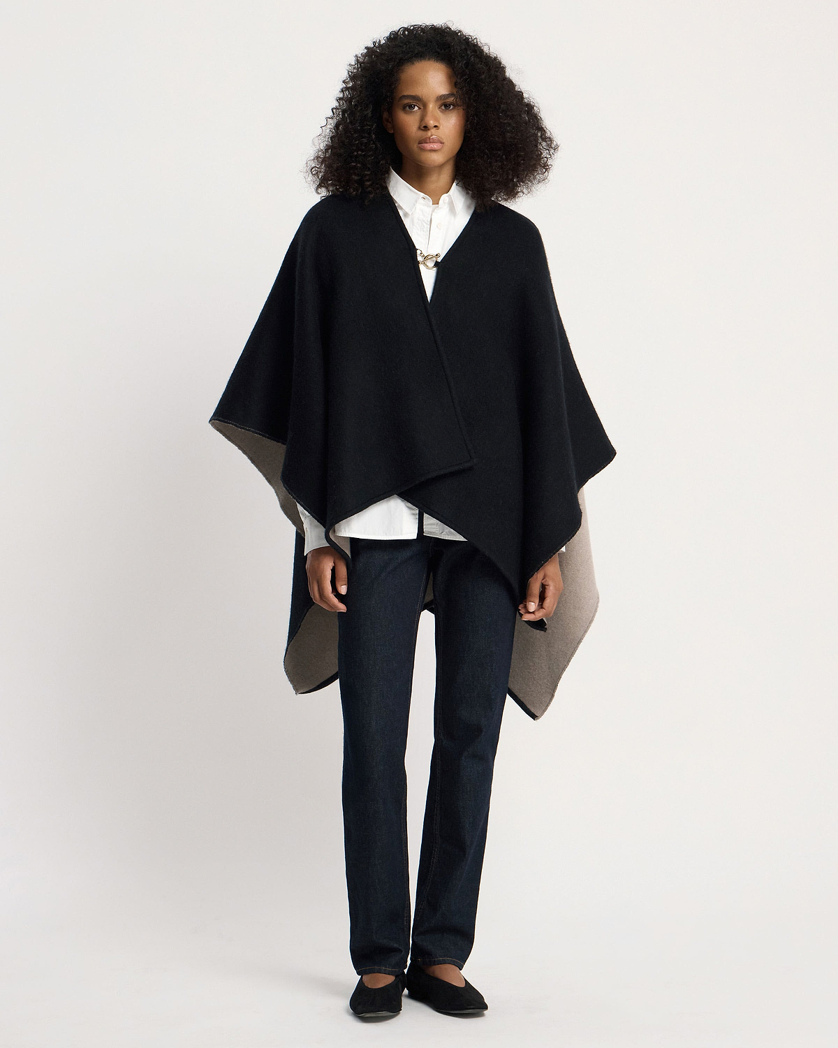 Woman wearing otter and black woven kite cape over white shirt and jeans.
