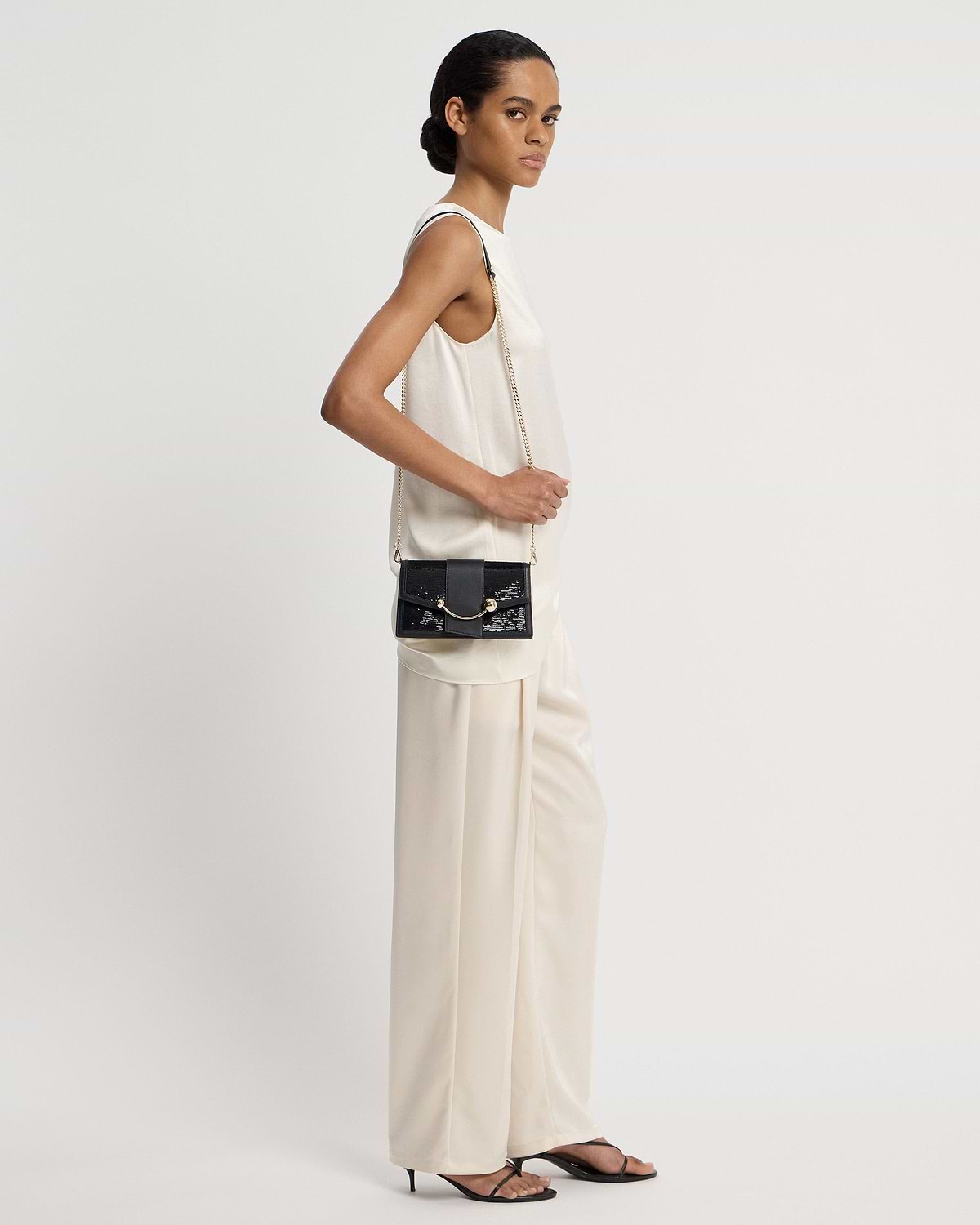 Model wearing a black sequin crescent-on-a-chain shoulder bag with gold chain.