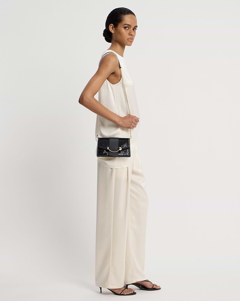 Model wearing a black sequin crescent-on-a-chain shoulder bag with gold chain.