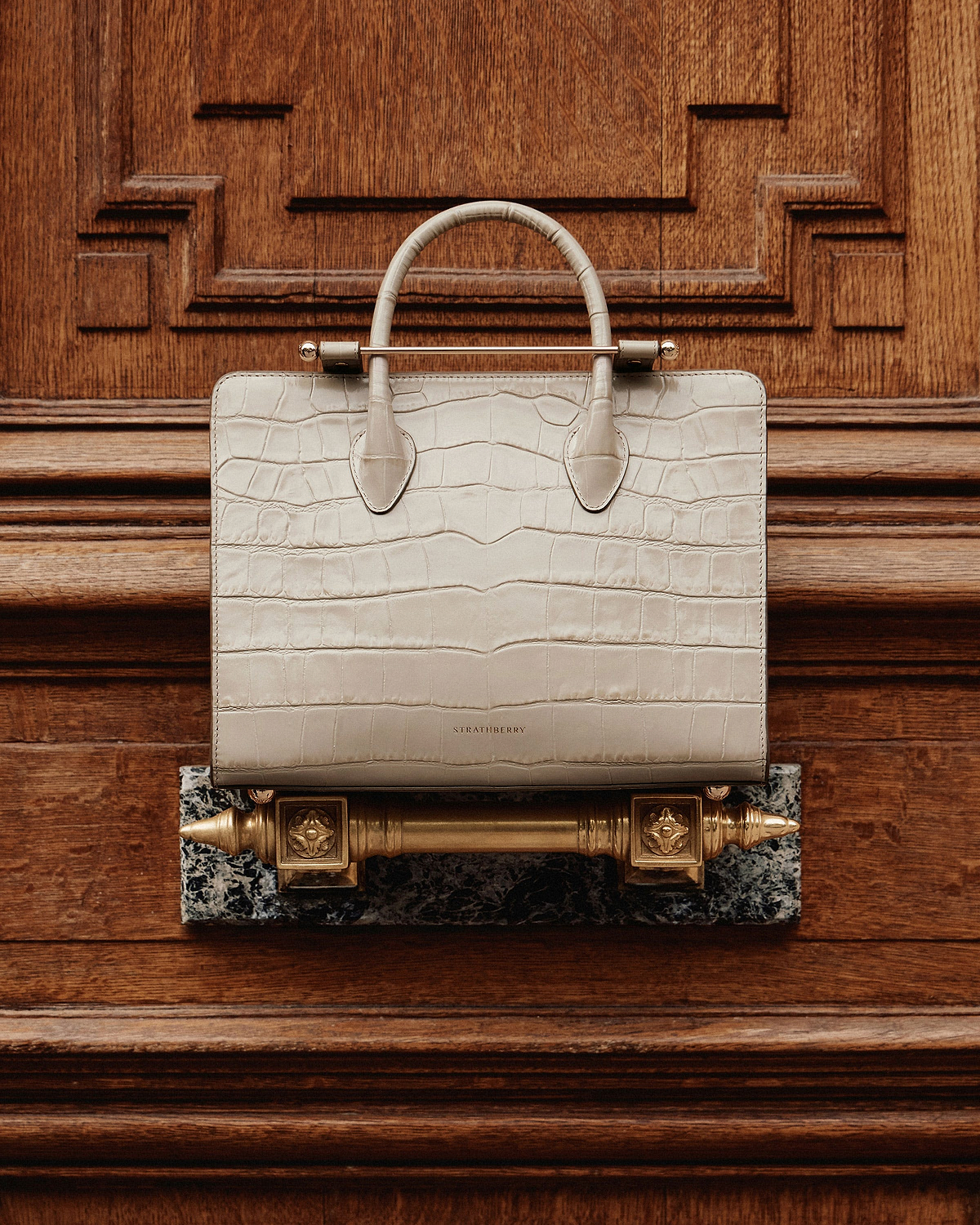 Cream croc-embossed Strathberry midi tote with twin handles on carved wood.