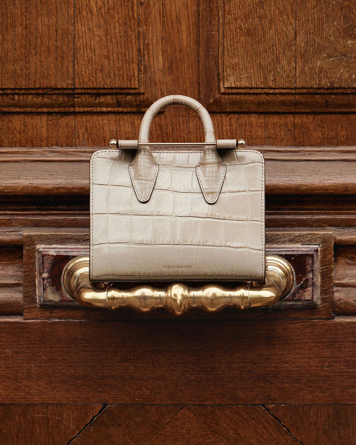 Strathberry nano tote in croc leather on a wooden door handle.