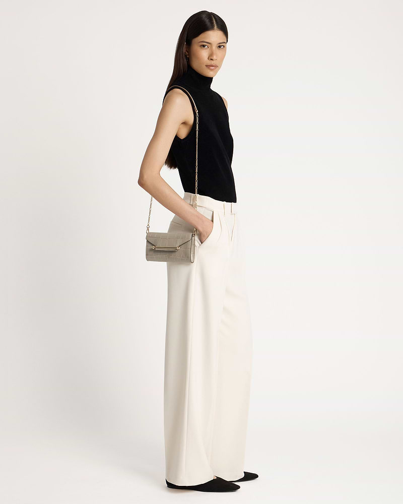 Woman wearing a black sleeveless top and cream trousers, shoulder croc chain wallet.