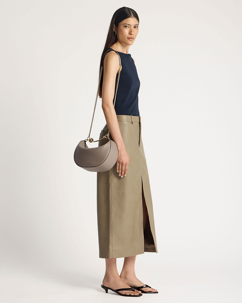 Model wearing a taupe crescent moon shoulder bag with gold chain strap