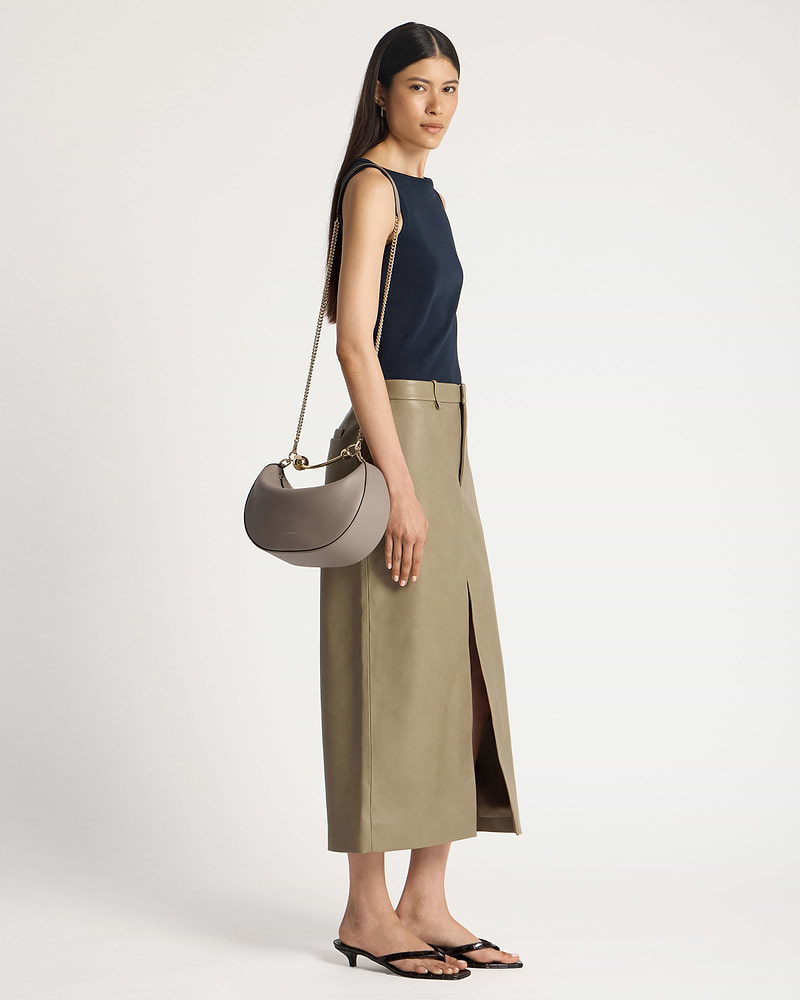 Model wearing a taupe crescent moon shoulder bag with gold chain strap