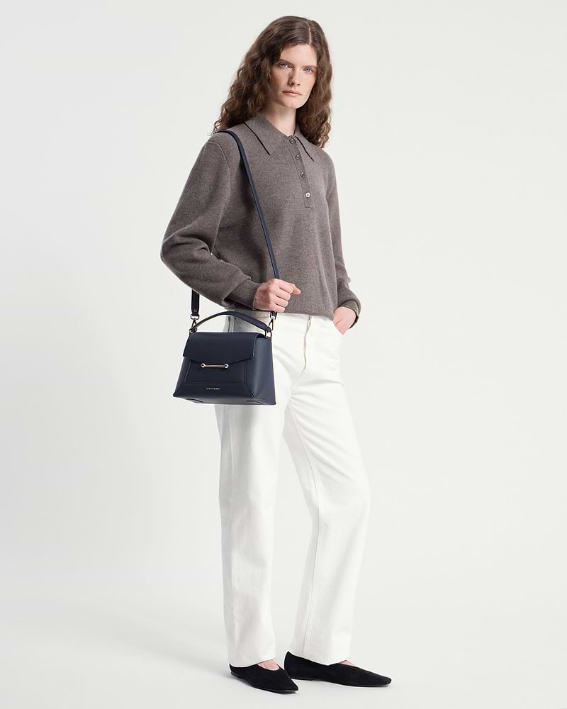 Model wearing grey sweater and white trousers holding navy Strathberry mosaic bag