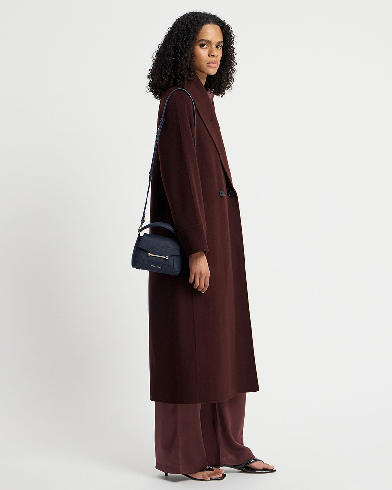 Woman in burgundy coat carrying navy Strathberry Mosaic Nano shoulder bag.