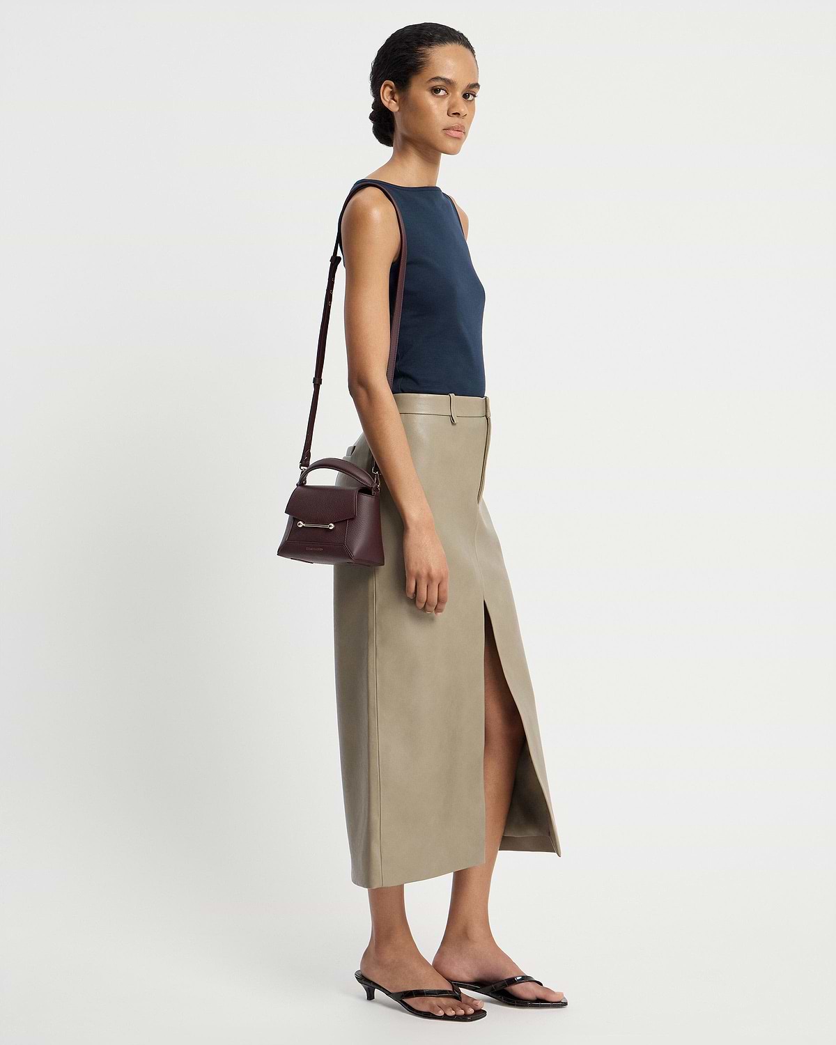 Model wearing navy top and beige skirt carrying burgundy Mosaic Nano bag with shoulder strap