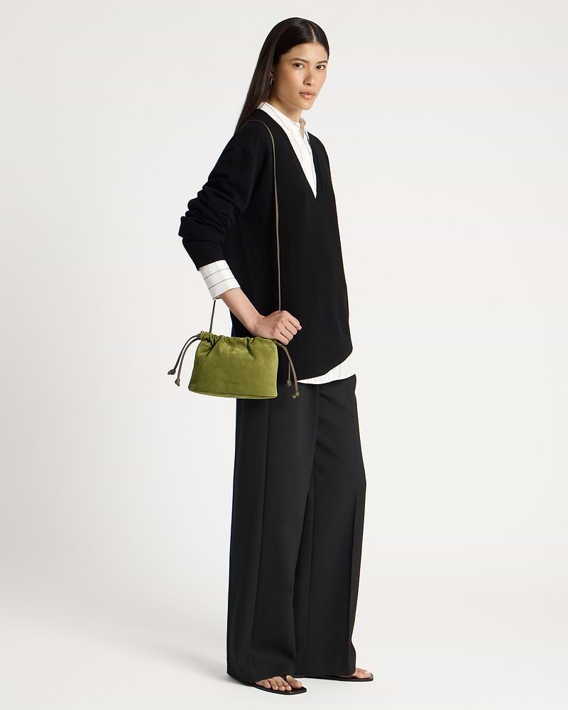 Model wearing black V-neck sweater holds lime suede drawstring bag at her hip.