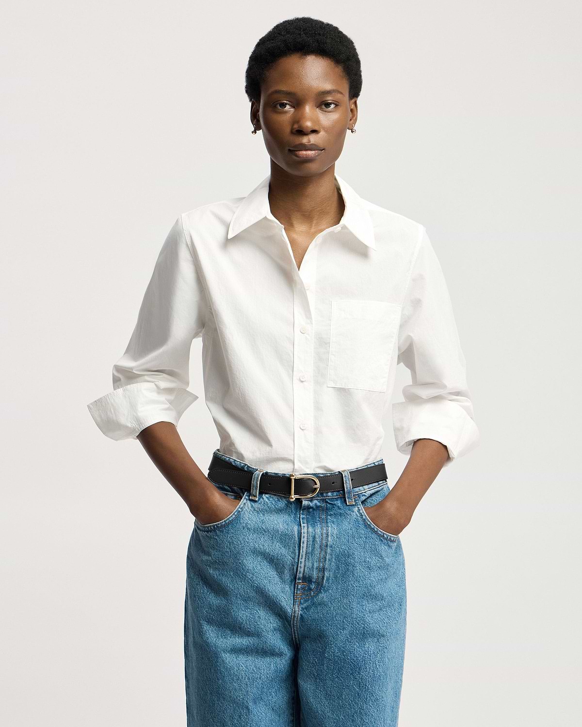 Model wearing black leather belt with gold buckle, white shirt and blue jeans.
