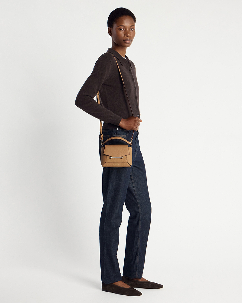 Model wearing a small caramel pebbled leather crossbody bag with top handle and shoulder strap.