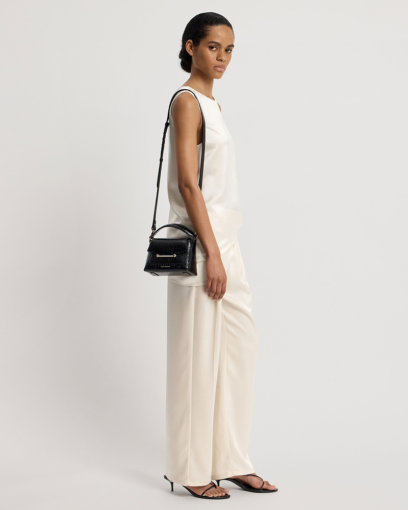 Model in sleeveless white top and cream trousers carrying small black croc bag