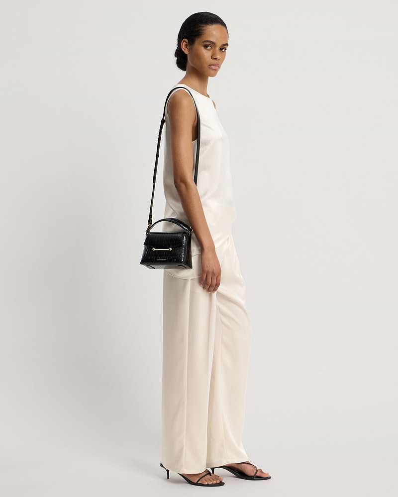 Model in sleeveless white top and cream trousers carrying small black croc bag
