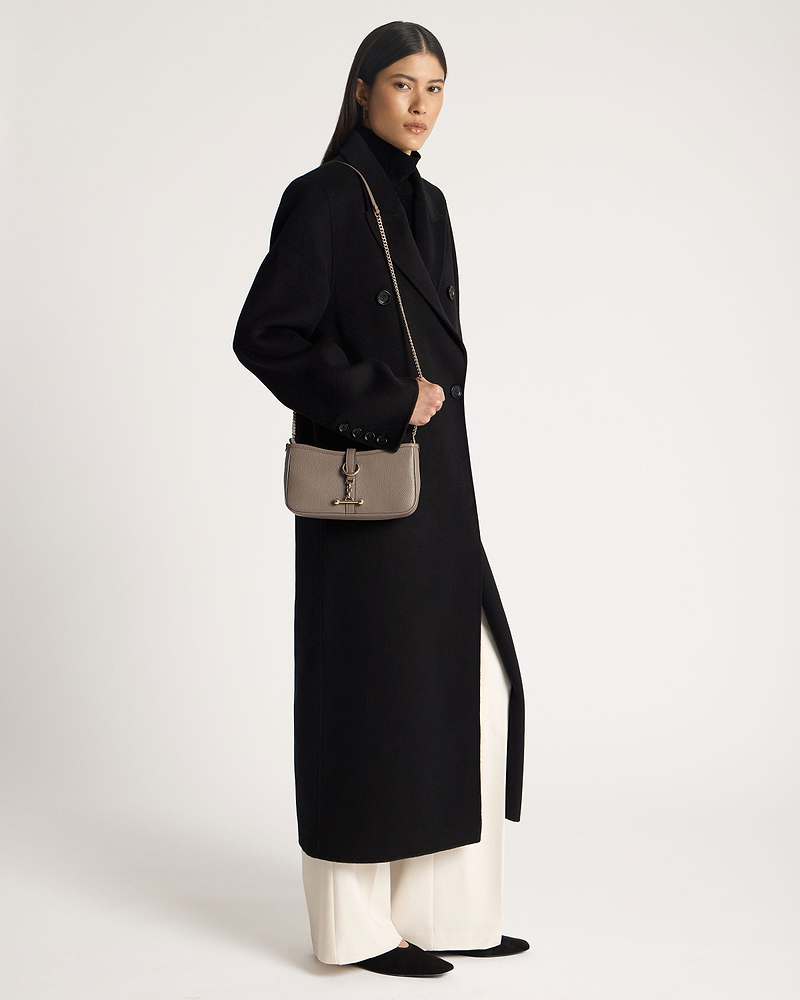Model in black coat holding taupe Kite on a Chain bag with gold chain strap.