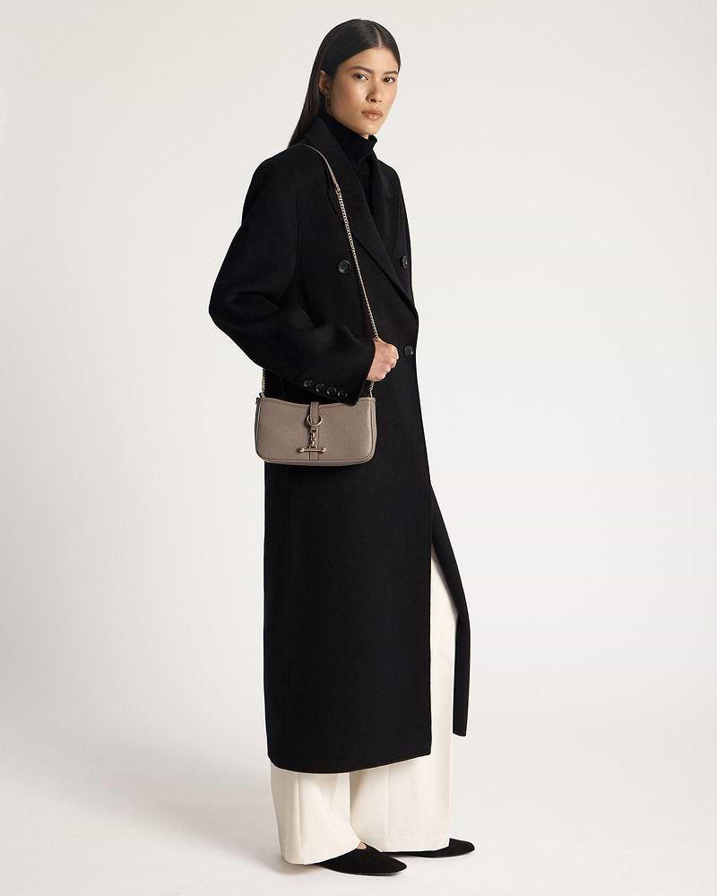 Model in black coat holding taupe Kite on a Chain bag with gold chain strap.