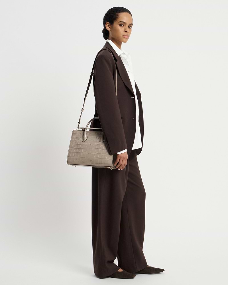 Woman in brown suit carrying a croc-effect midi tote bag at her side.