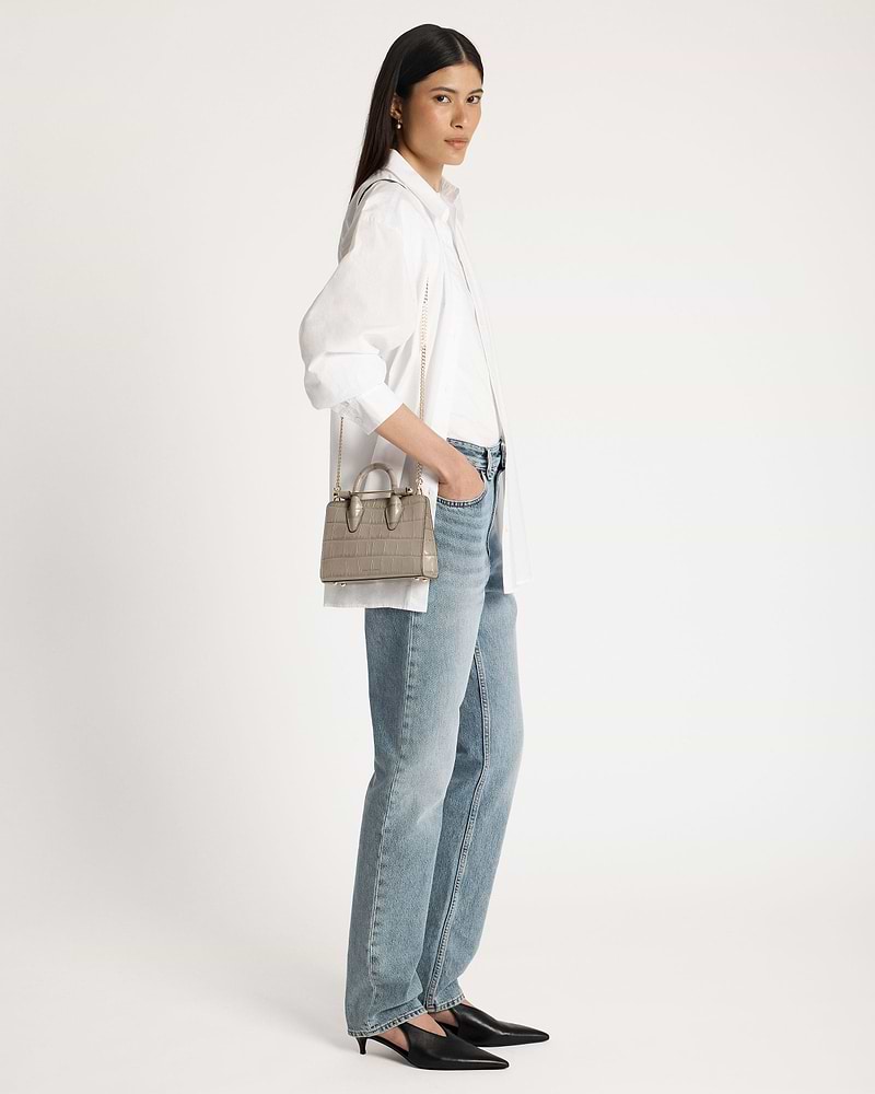 Woman wearing white shirt and jeans carrying a croc nano tote bag.