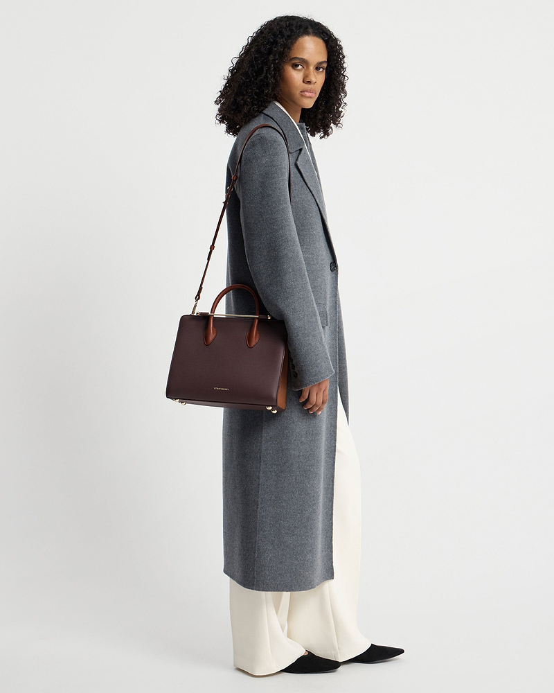 Model wearing grey coat holding Strathberry midi tote in burgundy, walnut, chestnut.