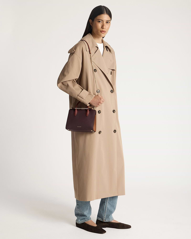 Model in beige trench coat holding burgundy, chestnut and walnut mini tote bag.
