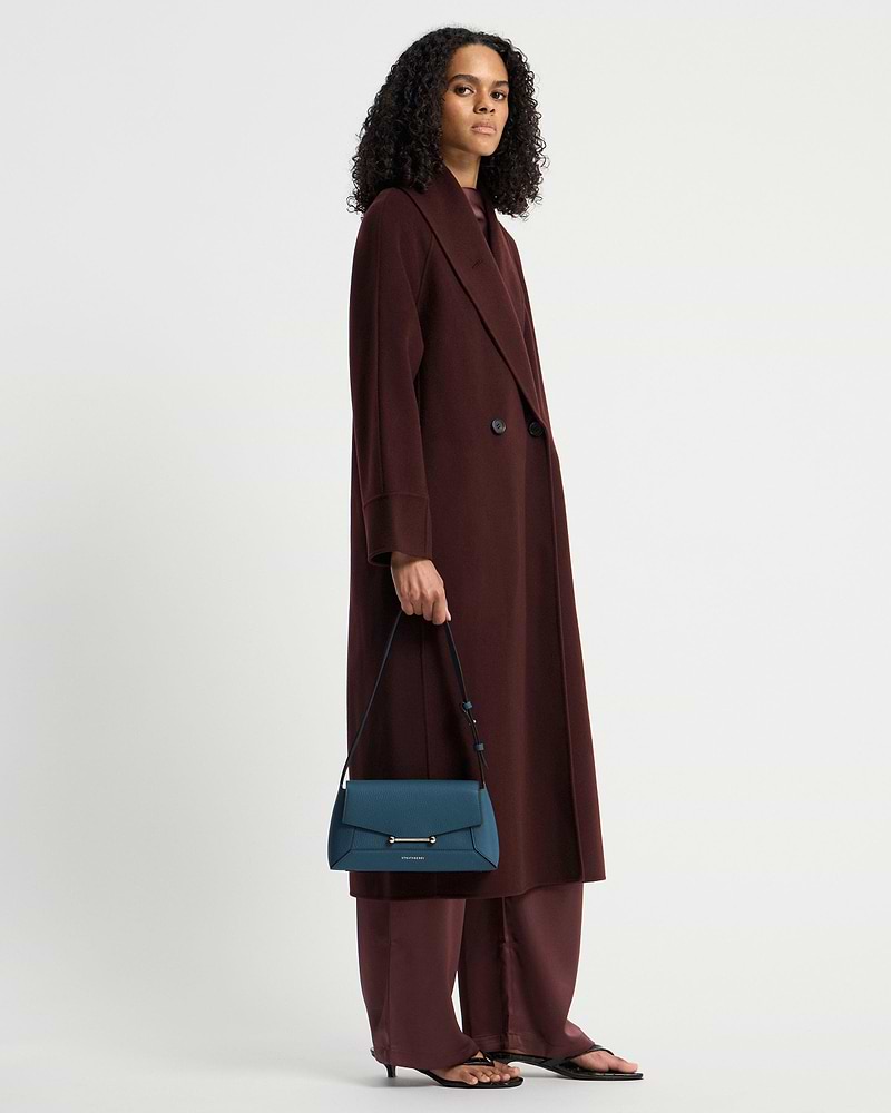 Model wearing long burgundy coat holding Loch Blue Mosaic Shoulder bag by Strathberry.