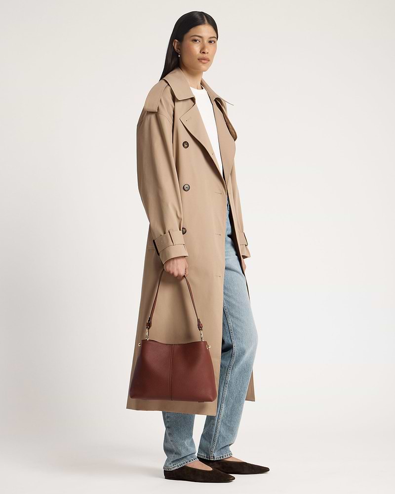Woman in trench coat holding a walnut Lana hobo leather bag by the handle.