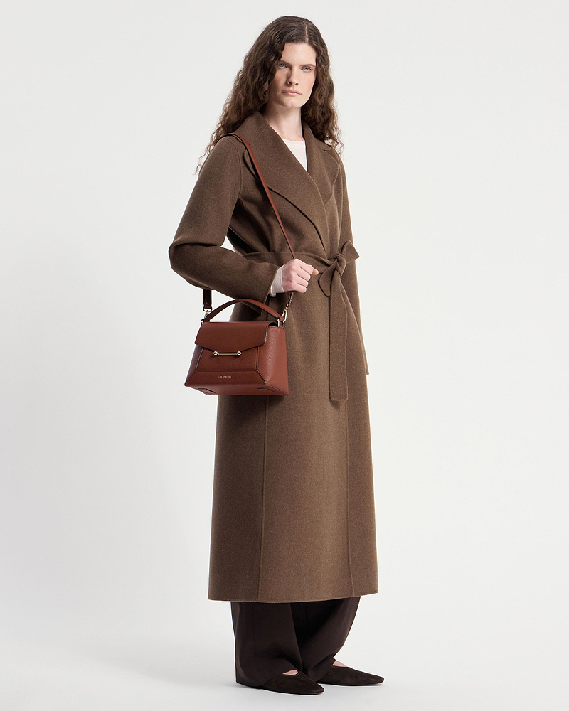 Model wearing a brown long coat holding a walnut mosaic bag by the strap.