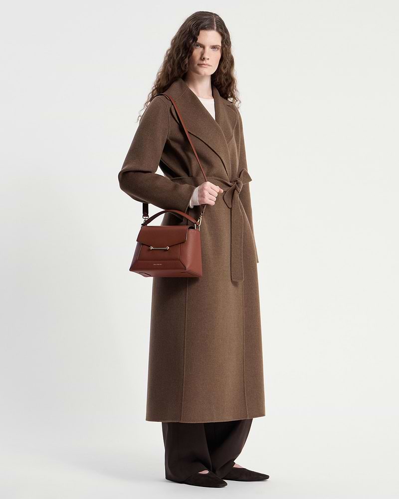 Model wearing a brown long coat holding a walnut mosaic bag by the strap.