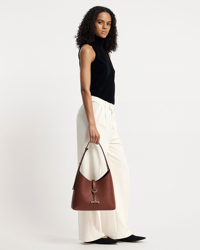 Woman in black sleeveless top and cream trousers holding a walnut Kite Hobo bag