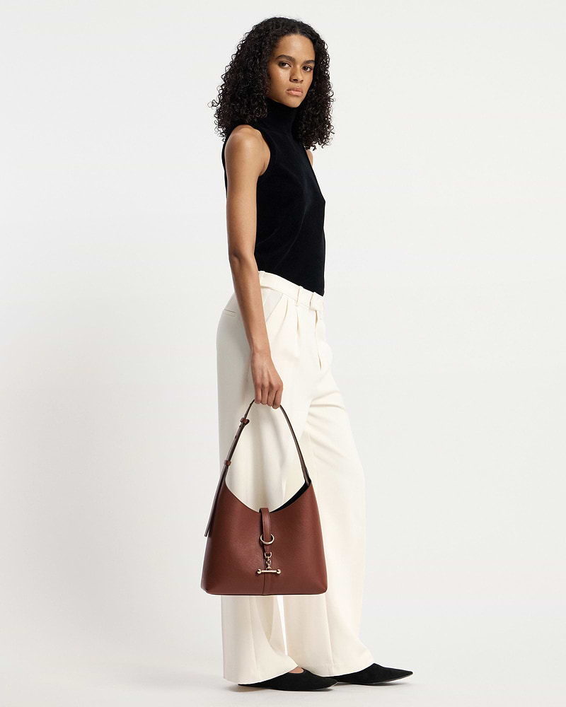 Woman in black sleeveless top and cream trousers holding a walnut Kite Hobo bag