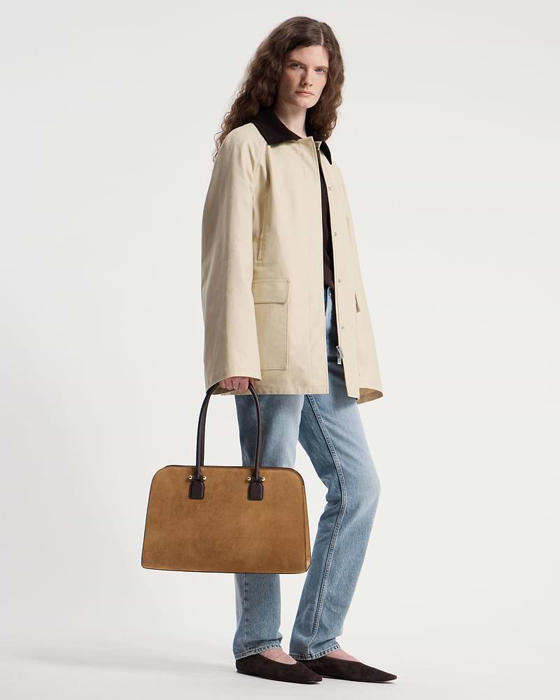 Model carrying toffee suede tote with espresso handles, wearing beige coat and blue jeans.
