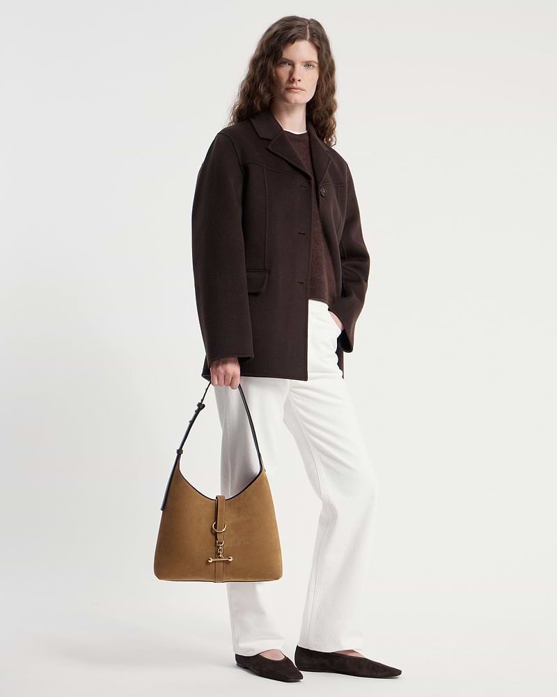 Model wearing dark coat and white trousers holding toffee suede and espresso Kite Hobo bag.