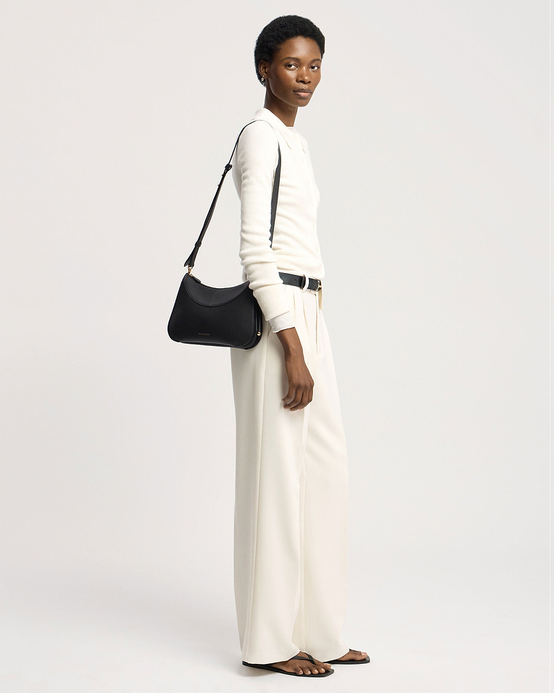 Model wearing cream top and trousers carrying a black shoulder bag over her shoulder.