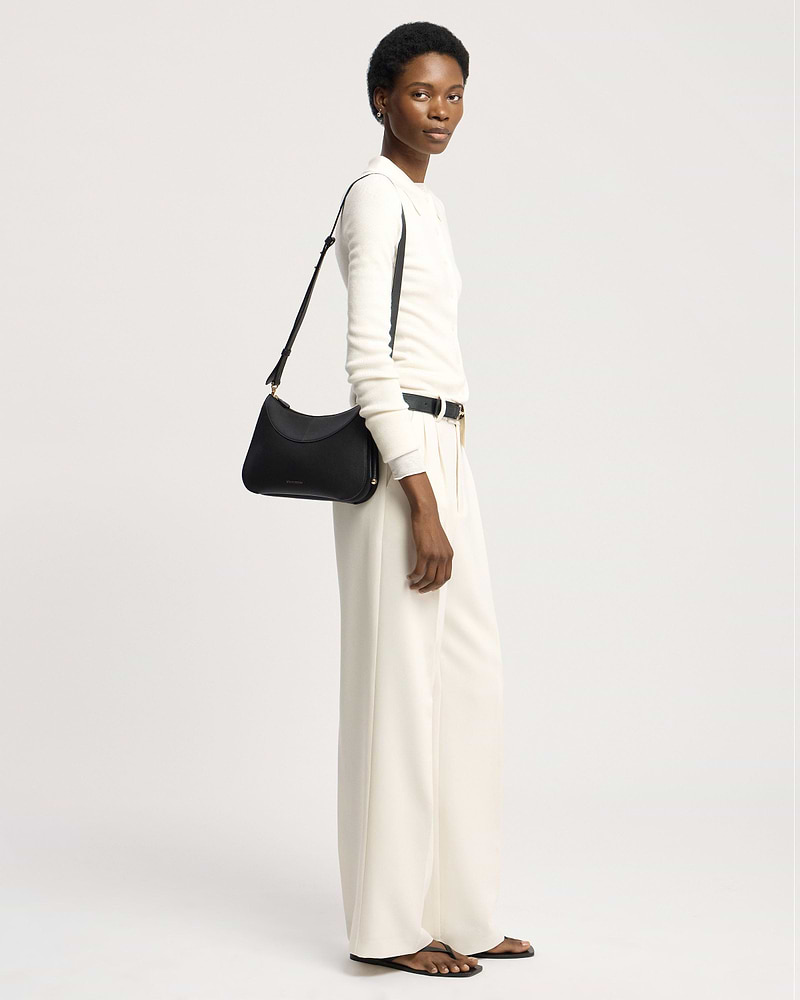 Model wearing cream top and trousers carrying a black shoulder bag over her shoulder.
