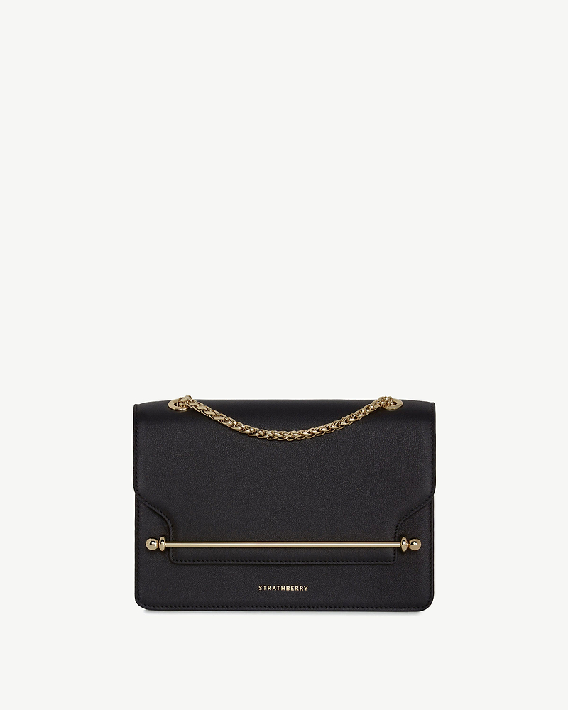 Strathberry east-west bag in black with gold chain handle and metal bar.