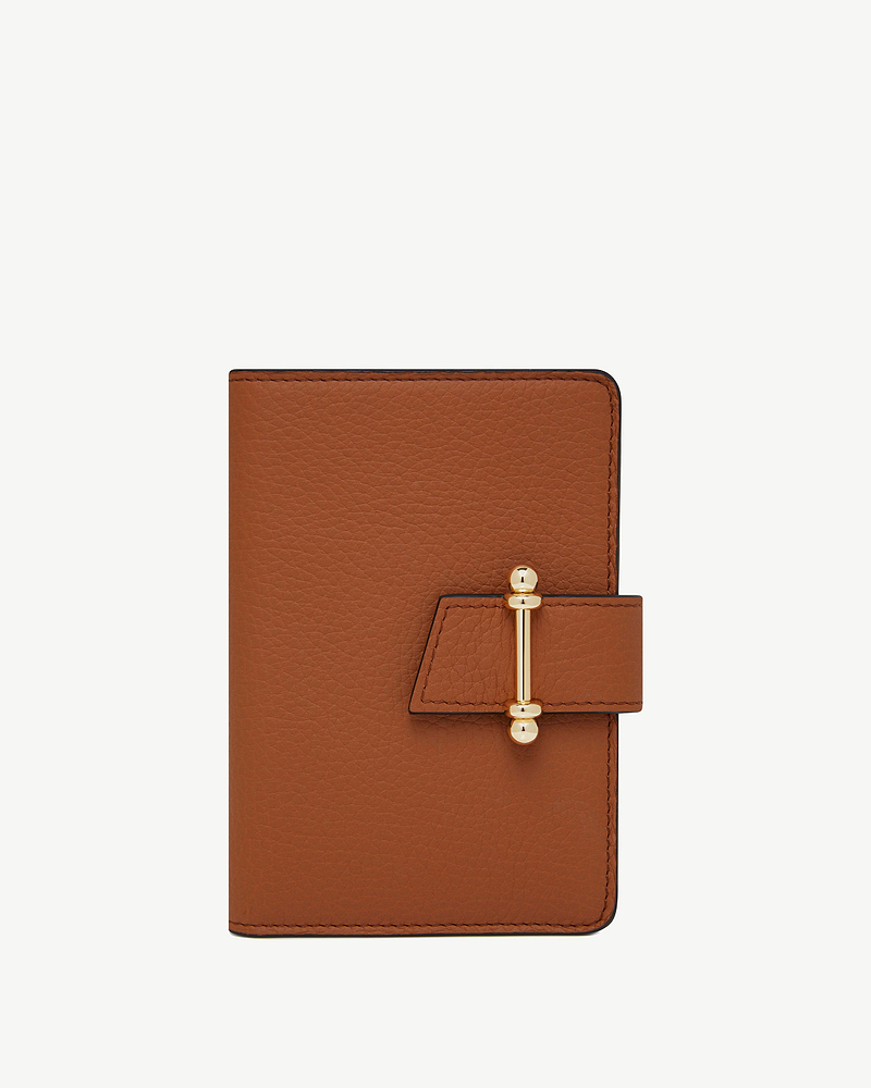 Tan leather passport holder with gold bar clasp on white background