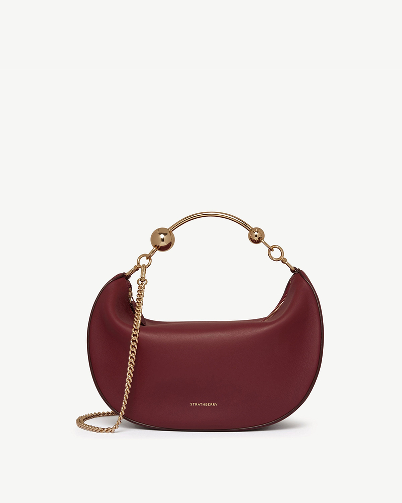 Strathberry Crescent Moon oxblood leather bag with gold metal handle and chain strap.