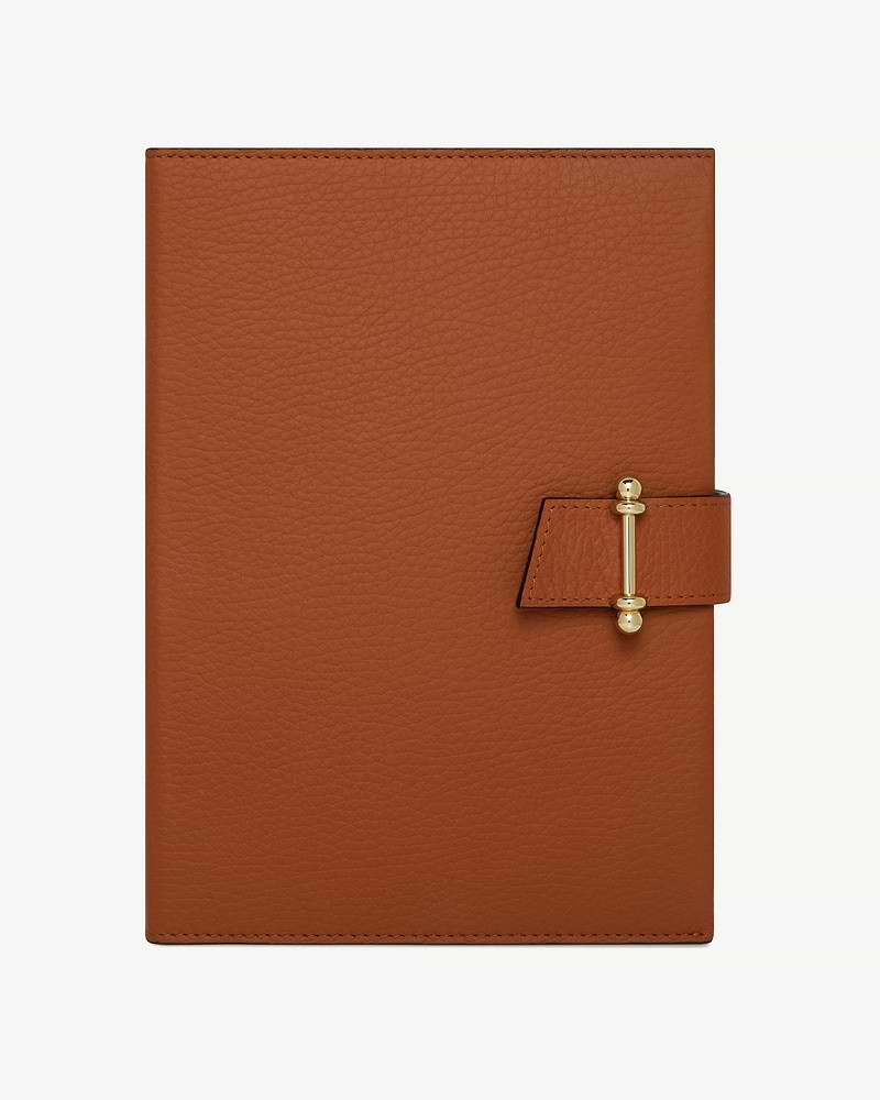 Tan leather notebook with gold bar clasp and pebble-grain texture.