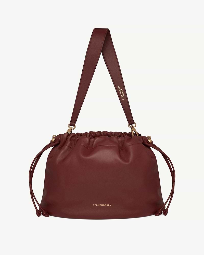 Oxblood Strathberry Charlotte midi drawstring bag with wide shoulder strap.