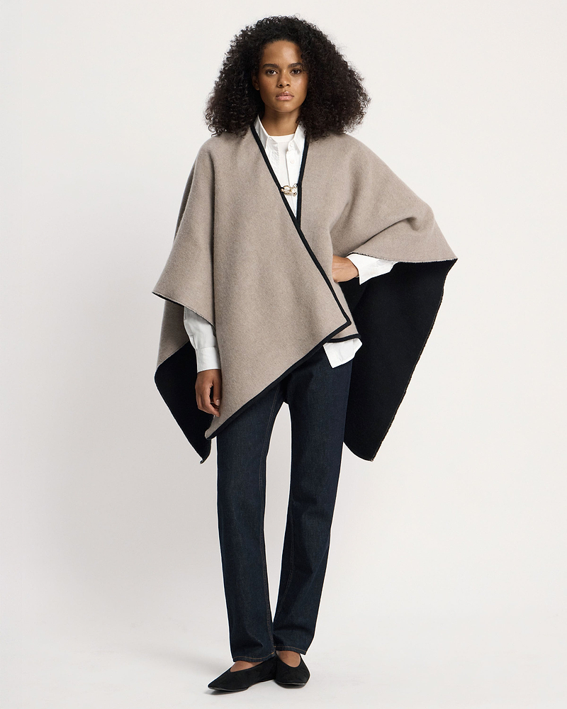 Model wearing otter and black woven cape over white shirt and dark jeans.