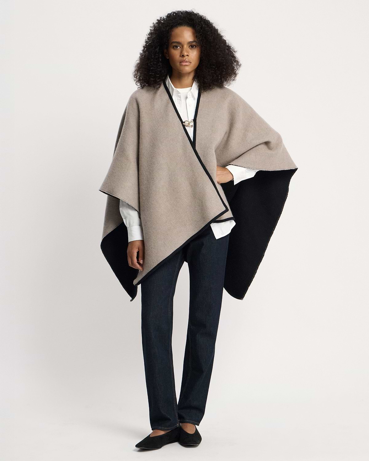 Model wearing otter and black woven cape over white shirt and dark jeans.