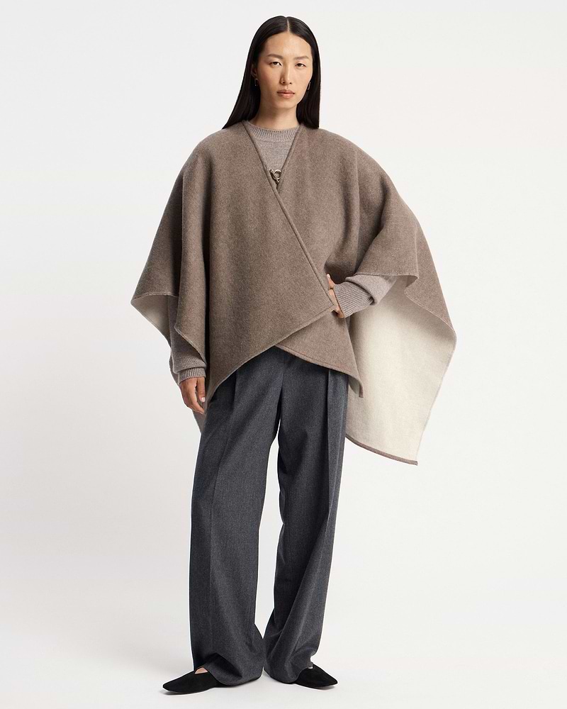 Model wearing a taupe kite woven cape over a grey sweater and trousers.