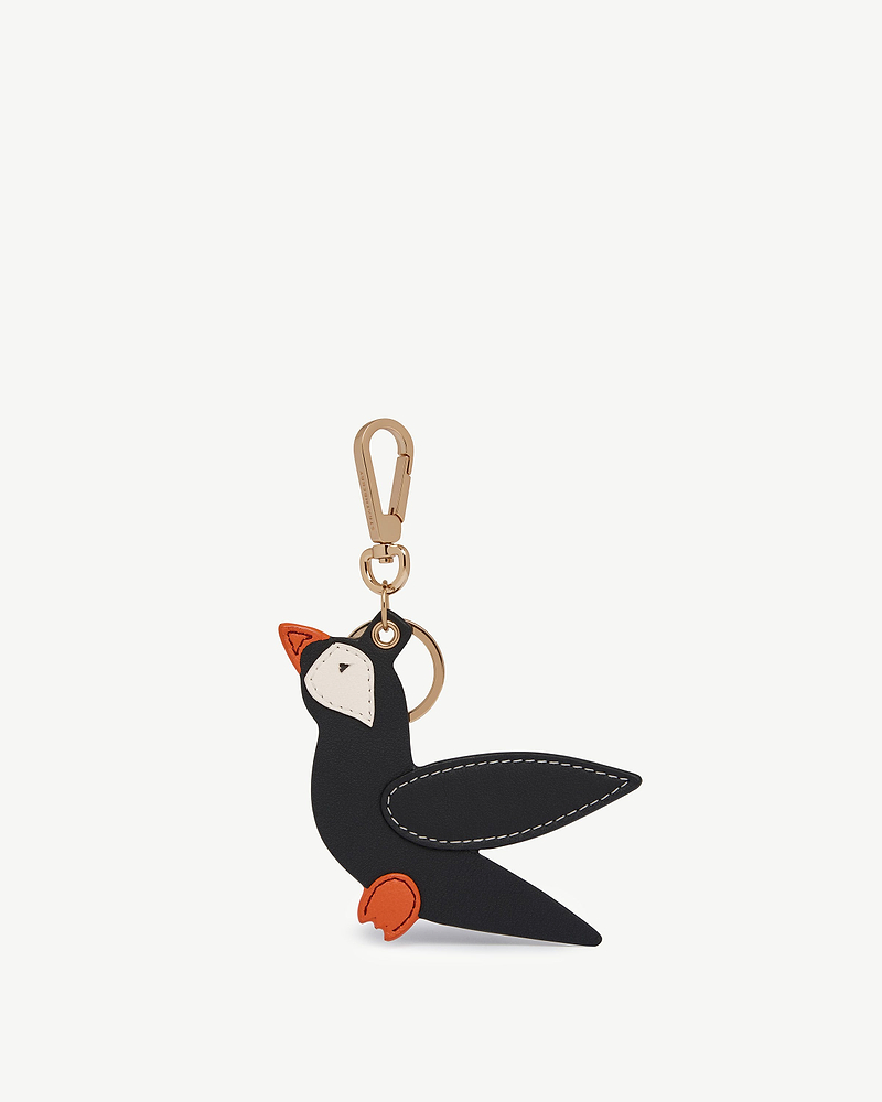 Puffin-shaped black leather bag charm with vanilla face, marmalade beak and feet, gold clip.