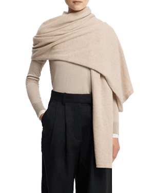 Model wearing an oat-coloured travel wrap draped over one shoulder with beige jumper.