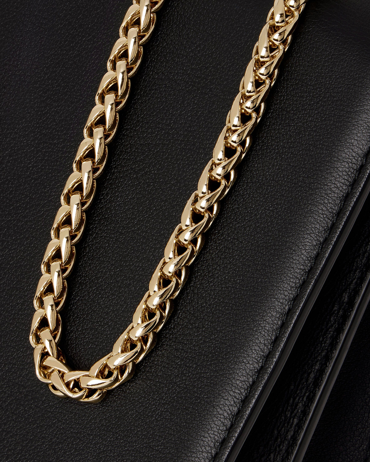 Black east-west bag showing pebbled leather and gold chain strap.