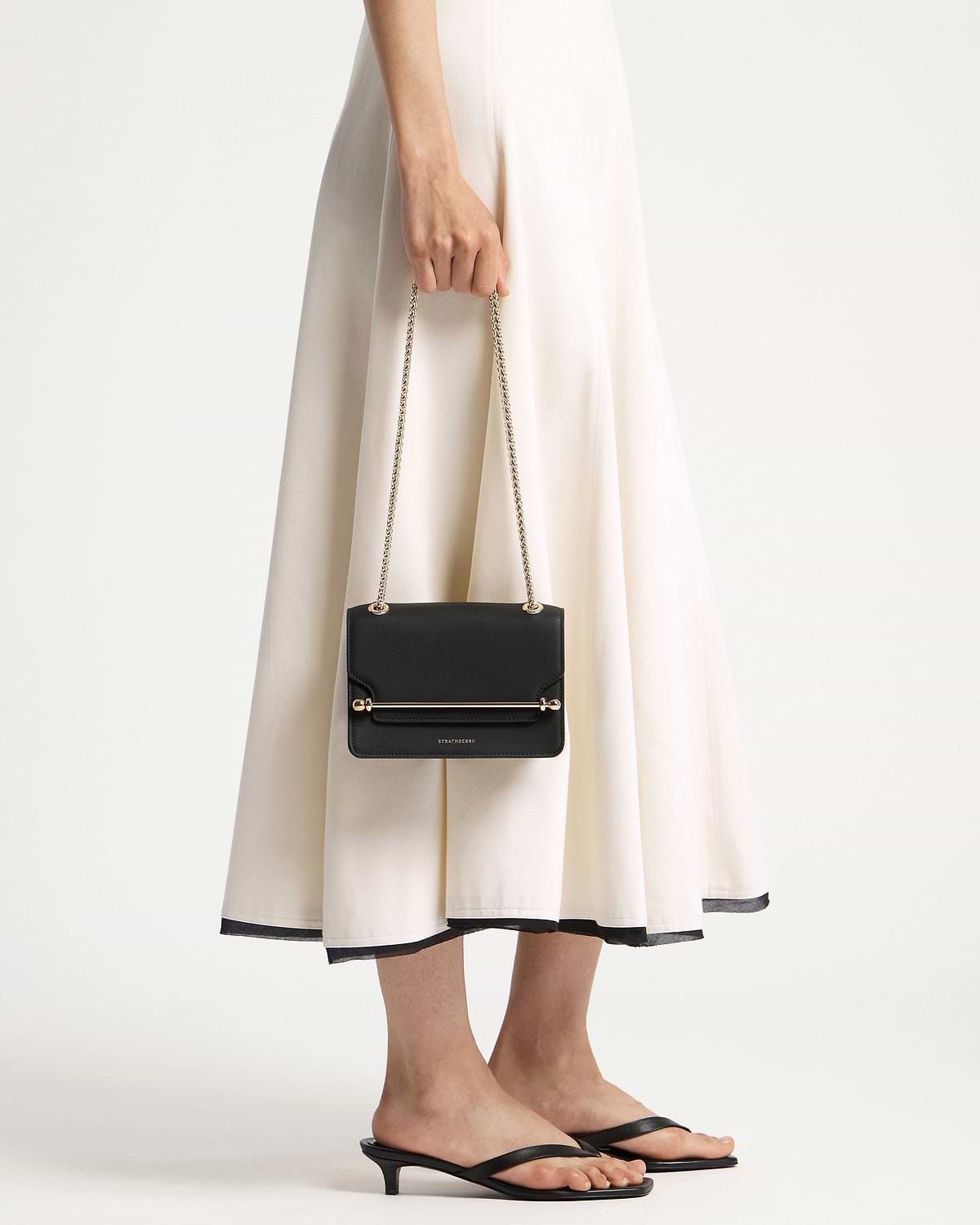 Model holding black Strathberry East/West Mini bag with gold chain strap.