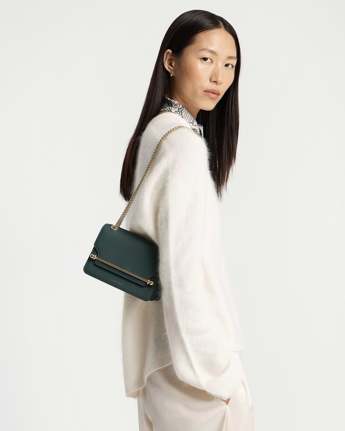 Woman wearing bottle green East/West Mini shoulder bag with gold bar detail.